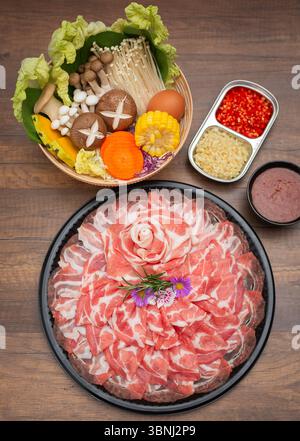 Ein wunderschön gestaltetes japanisches Hot Pot (Shabu Shabu) Set mit dünn geschnittenem Schweinefleisch, das in Blütenform auf einem schwarzen Tablett angeordnet ist, umgeben von Stockfoto