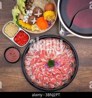 Ein wunderschön gestaltetes japanisches Hot Pot (Shabu Shabu) Set mit dünn geschnittenem Schweinefleisch, das in Blütenform auf einem schwarzen Tablett angeordnet ist, umgeben von Stockfoto