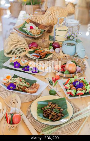 Ein wunderschön gestaltetes traditionelles thailändisches Essensset auf einem Holztisch mit natürlichem Licht. Das Bild zeigt eine Vielzahl authentischer thailändischer Gerichte in Stockfoto