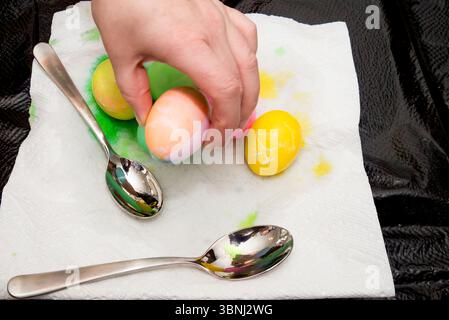Eine Hand, die ein Osterei aus einem Haufen frisch gefärbter Eier aufnimmt. Stockfoto