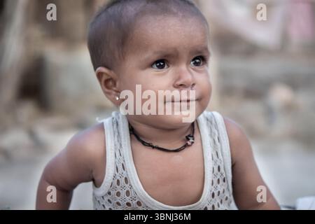 Niedliches Indianerbaby in ärmellosem weißem Oberteil mit Halskette und Ohrringen, das im Freien nachdenklich aussieht Stockfoto