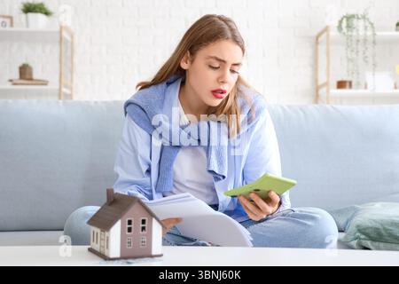 Junge Frau mit Taschenrechner und Rechnungen zu Hause. Preissteigerungskonzept Stockfoto