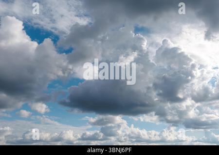 Ein landschaftlich schöner Himmel mit einer Mischung aus dunklen und flauschigen Wolken, die eine dramatische und dynamische Atmosphäre mit blauen Flecken schaffen. Stockfoto