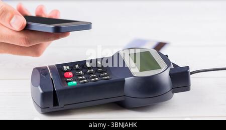 Das flache POS-Terminal liegt auf einer hellen Holzoberfläche auf, mit eingelegter Karte und Smartphone-Abtastung Stockfoto