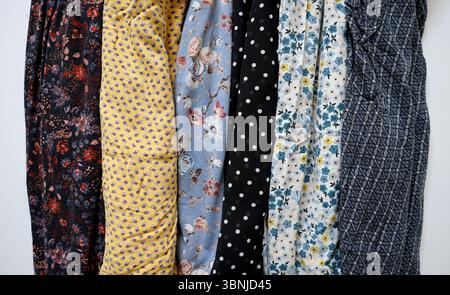Foto von verschiedenen bedruckten Stoffen. In vertikalen Streifen auf weißem Hintergrund angeordnet. Verschiedene Farben und Muster. Blumenmuster, Punktmuster, Ornamente. Blau, gelb, braun, weiß, schwarz. Kleidung. Stockfoto