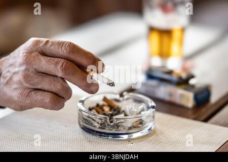 Die Hand eines rauchenden Mannes oder einer rauchenden Frau auf einem Tisch führte einen Aschenbecher mit Bier vom Fass in einem Pub. Stockfoto