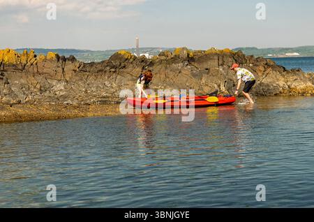 Helens Bay Co.Down Nordirland 10. Mai 2025 - zwei Menschen in hellen Kleidern starten ein oranges Kajak in den Belfast Lough Stockfoto