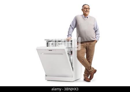 Lächelnder reifer Mann lehnt sich auf einen Geschirrspüler mit Geschirr isoliert auf weißem Hintergrund Stockfoto