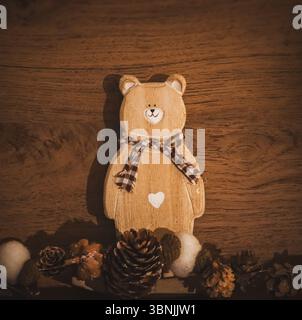 Ein gemütliches, vertikales Stillleben mit rustikaler Holzbärendekoration mit kariertem Schal und weißem Herz. Tannenzapfen und unscharfe Elemente. Stockfoto