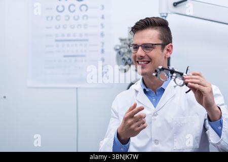 Versuchsrahmen auf Untersuchungstisch in der Optometrie-Klinik sitzend, mit Phoropterarm und verschwommener Snellen-Chart Stockfoto
