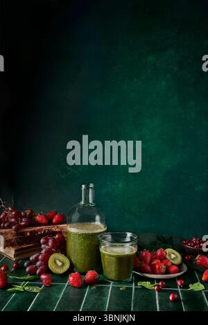 Ein erfrischender grüner Spinatsaft in einer Glasflasche mit einer Tasse, umgeben von frischen Erdbeeren, Kirschen und Trauben. Perfekt für gesundheitsbewusste Menschen Stockfoto
