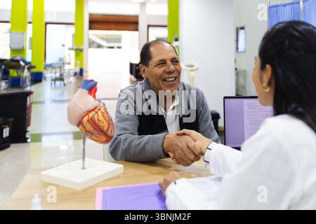 Ein älterer männlicher Patient wird von einer jungen Ärztin im Krankenhaus aufmerksam betreut. Die Interaktion hebt Mitgefühl und Beruf hervor Stockfoto
