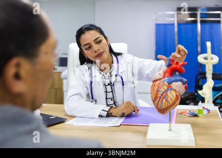 Eine fürsorgliche junge Ärztin betreut einen älteren männlichen Patienten in einem warmen und professionellen lateinamerikanischen Krankenhaus-Setting und zeigt aufmerksame Heilung Stockfoto