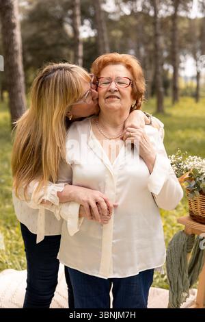 Ein berührender Moment zwischen Mutter und Tochter, festgehalten in einer ruhigen Umgebung im Freien. Die Tochter küsst ihre Mutter liebevoll auf die Wange, Symbolizi Stockfoto
