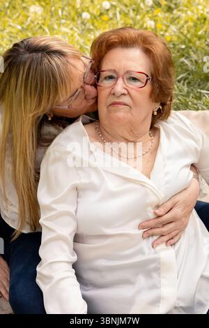 Ein berührender Moment zwischen Mutter und Tochter, die die gemeinsame Zeit in einem sonnigen Park genießen. Die Tochter umarmt ihre Mutter liebevoll und küsst sie Stockfoto