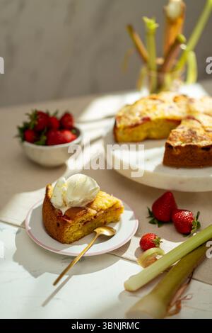 Genießen Sie diesen hausgemachten Rhabarberkuchen mit Erdbeeren, der wunderschön mit einem Klecks Vanilleeis präsentiert wird. Perfekt für jeden Dessertliebhaber oder Backen Stockfoto