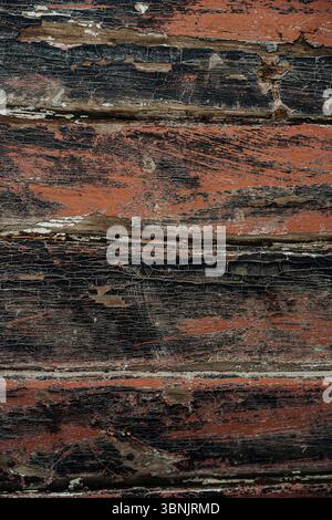 Nahaufnahme einer verwitterten Holzoberfläche mit schwarzer und roter abblätternder Farbe. Die Textur hat ein altertümliches, rustikales Erscheinungsbild, ideal für Hintergründe oder kunstwerke Stockfoto