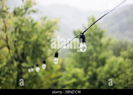 Lichterketten hängen zart in der nebeligen Bergkulisse und fangen die ruhige Atmosphäre eines regnerischen morgens ein. Wassertropfen haften an den Zwiebeln, äh Stockfoto