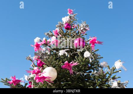 Weihnachtsbaum mit leuchtenden rosafarbenen, weißen und silbernen Ornamenten vor einem klaren blauen Himmel. Die festlichen Dekorationen sorgen für einen fröhlichen Urlaub Stockfoto
