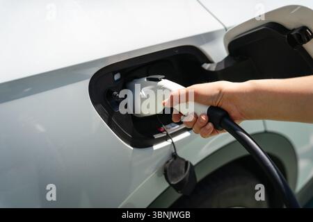 Nahaufnahme einer Person, die ein Ladekabel an ein Elektrofahrzeug in einer städtischen Umgebung anschließt und alternative Transportlösungen für zeigt Stockfoto