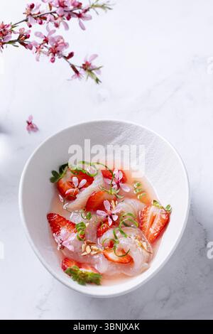 Von oben ein lebhaftes Ceviche, garniert mit frischen Erdbeeren und Mandelblüten in einer weißen Schüssel, schafft ein optisch exquisites und appetitliches Dinner Stockfoto