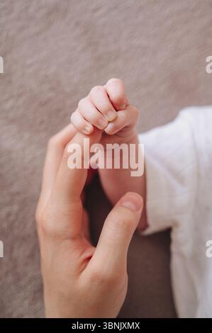 Eine Mutter hält liebevoll die winzige Hand ihres einmonatigen Neugeborenen und symbolisiert die Zärtlichkeit und Verbindung zwischen ihnen. Die intime Momentaufnahme Stockfoto