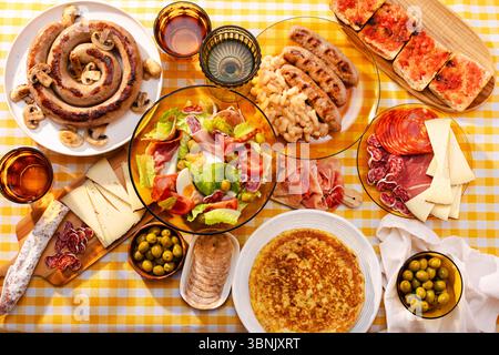 Ein lebhafter Tisch mit einem traditionellen katalanischen Salat, Botifarra mit Pilzen, Oliven, spanischer Marmelade, Käse, und eine Tortilla mit Kartoffeln Stockfoto