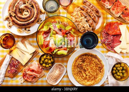 Ein lebhafter Tisch mit einem traditionellen katalanischen Salat, Botifarra mit Pilzen, Oliven, spanischer Marmelade, Käse, und eine Tortilla mit Kartoffeln Stockfoto