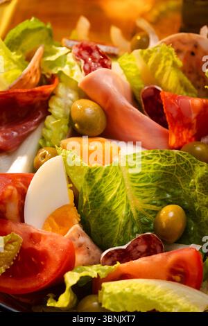 Nahaufnahme eines farbenfrohen katalanischen Salats mit knusprigem Salat, Reifen Tomaten, hart gekochten Eiern, Oliven und verschiedenen Wurstsorten, die ein frisches und kreieren Stockfoto