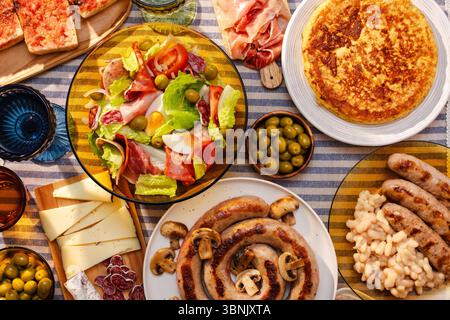 Ein lebhafter Tisch mit einem traditionellen katalanischen Salat, Botifarra mit Pilzen, Oliven, spanischer Marmelade, Käse, und eine Tortilla mit Kartoffeln Stockfoto