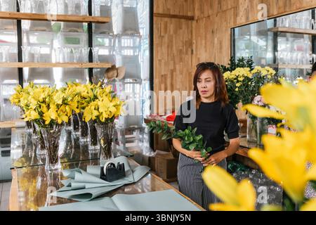 Eine engagierte Floristin auf Bali arrangiert leuchtend gelbe Blumen mit Fokus und Präzision und zeigt ihre Leidenschaft für Blumendesign in einem bezaubernden Holzinnenraum Stockfoto