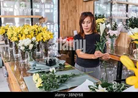 Eine engagierte Floristin auf Bali arrangiert geschickt wunderschöne Blumensträuße in ihrem lebhaften Geschäft. Umgeben von frischen Blumen zeigt sie Kreativität und Passi Stockfoto