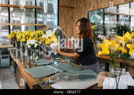 Eine engagierte Floristin auf Bali arrangiert in ihrem charmanten Geschäft akribisch einen atemberaubenden Blumenstrauß aus gelben und weißen Blumen und zeigt ihre Kreativität Stockfoto