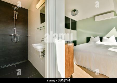 Ein stilvolles Hotelzimmer mit modernem Bad mit Dusche und komfortablem Schlafbereich mit modernen Designelementen Stockfoto