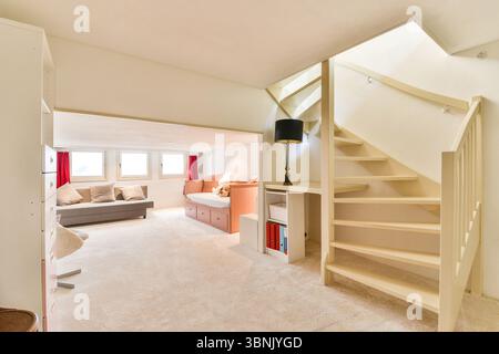 Geräumiges Zimmer mit komfortablen Sitzgelegenheiten, moderner Einrichtung und stilvollem Treppenhaus. Das Tageslicht und der weiche Teppich sorgen für ein einladendes und gemütliches Ambiente Stockfoto