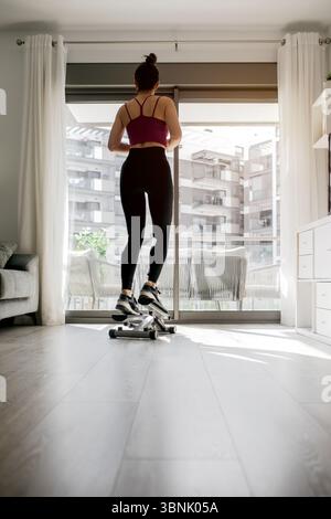Eine Frau trainiert zu Hause mit einer Stepmaschine. Sie konzentriert sich auf ihre Fitness-Routine in einem hellen Wohnzimmer, wobei sie Bewegung und Komfort in ihr ausbalanciert Stockfoto