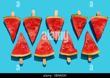 Erfrischende Wassermelonenstücke auf Stielen auf auffälligem blauem Hintergrund. Die leuchtend roten Früchte und die grüne Schale bilden einen scharfen Kontrast, was zu schaffen ist Stockfoto