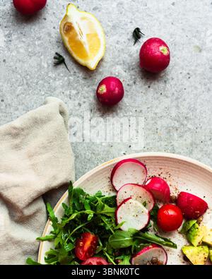 Ein lebhafter Sommersalat mit frischem Rucola, Radieschen, Kirschtomaten und Avocado. Perfekt garniert mit Zitrone, für eine erfrischende Atmosphäre Stockfoto