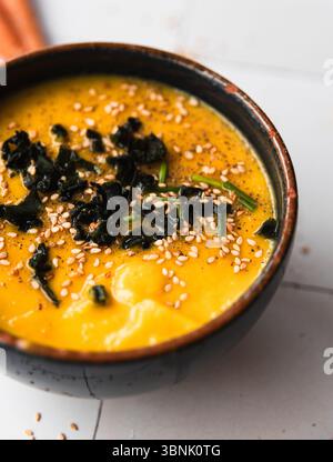 Eine warme, einladende Schüssel Kürbiscremesuppe, garniert mit zartem Wakam-Algen und bestreut mit Sesamsamen. Perfekt für ein gemütliches Essen, für Aufnahmen Stockfoto