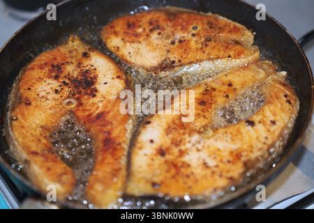 Nahaufnahme von drei brausenden Lachssteaks, die in der Pfanne gebraten werden und eine köstliche goldene Kruste zeigen. Perfekt, um frische und appetitliche Meeresfrüchte hervorzuheben Stockfoto