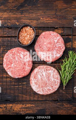 Gefrorene Fleischpasteten, bereit zum Grillen, Forcemeat von Schwein und Rindfleisch für Burger. Hölzerner Hintergrund. Draufsicht Stockfoto