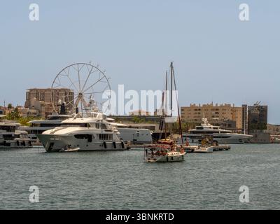 Luxuriöse Superyachten und ein Segelboot in Port Vell, Barcelona, mit dem Mirador de Port Vell (Riesenrad) im Hintergrund. Spanien. Stockfoto
