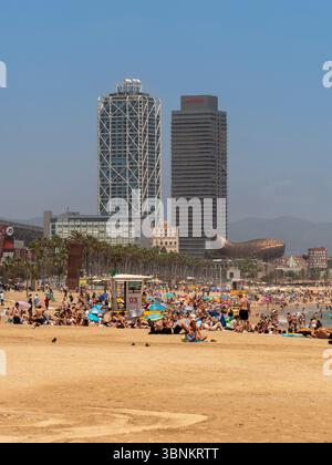 Sonnenanbeter haben den Barceloneta Beach im Sommer mit den berühmten Hotel Arts und den Wolkenkratzern des Mapfre Tower, die die Skyline der Stadt prägen. Stockfoto