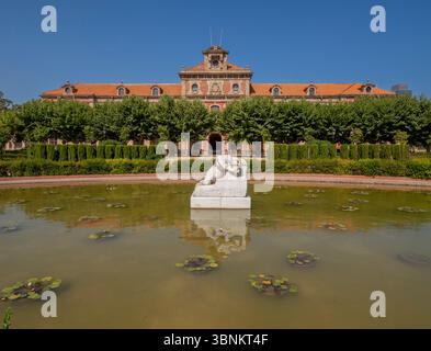 Das Gebäude des Parlaments von Katalonien im Parc de la Ciutadella, Barcelona, hinter einem Teich mit Seerosen und einer liegender Skulptur. Stockfoto