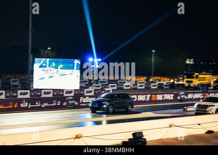 Motion Blur Drag Racing bei Nacht, bei dem Autos auf der Rennstrecke mit Zuschauern in der Nähe konkurrieren Stockfoto