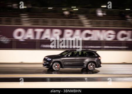 Motion Blur Drag Racing bei Nacht, bei dem Autos auf der Rennstrecke mit Zuschauern in der Nähe konkurrieren Stockfoto