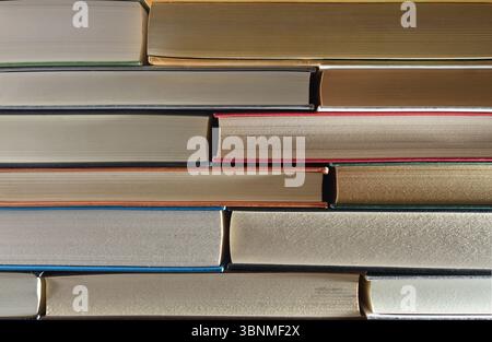 Detail eines Stapels von Büchern, der die Vorderkante auf einem Holzregal und einen dunklen isolierten Hintergrund zeigt. Vorderansicht. Stockfoto