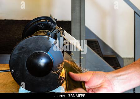 Mann, der ein Mähmesser schärft und Funken auf einer Werkstattmahlmaschine schaut Stockfoto