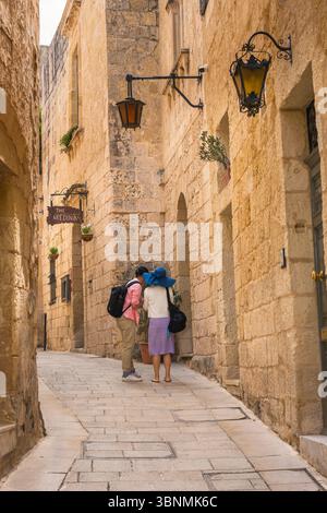 Touristenpaar Europa, Rückansicht zweier junger Menschen in einer engen Straße, die ihren Standort in der malerischen ummauerten Stadt Mdina, Malta, überprüfen. Stockfoto