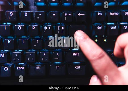 Nahaufnahme eines Fingers, der die Eingabetaste auf einer leuchtenden mechanischen Tastatur drückt. Stockfoto